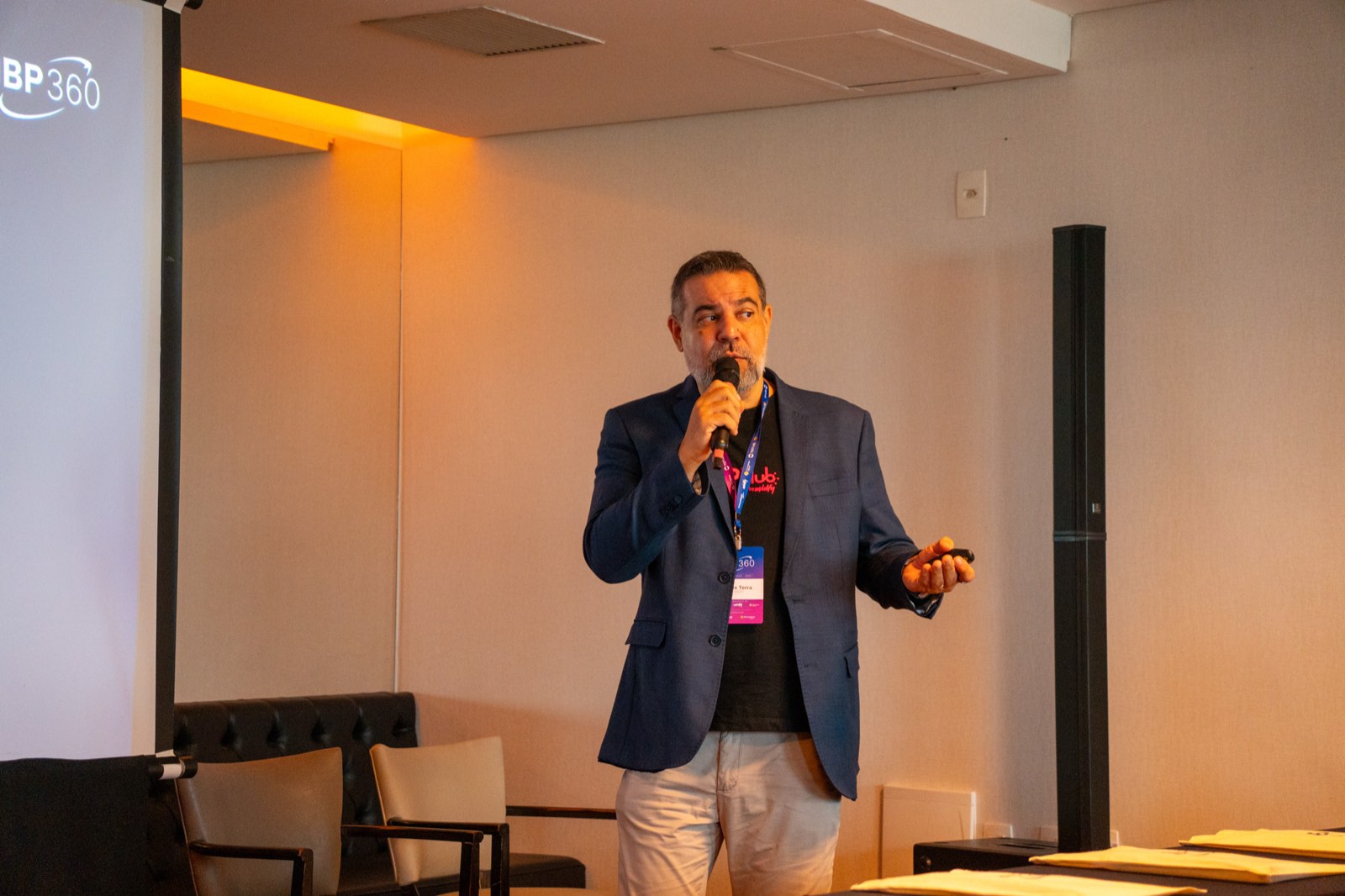Guilherme Auger, da Midfy, de blazer azul-marinho, fala ao microfone ao lado da projeção com a marca JBP360.